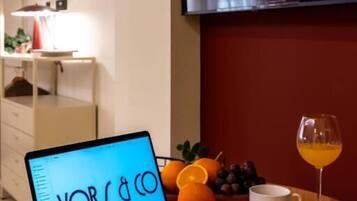 A laptop on a table with a glass of orange juice and a croissant, a white cup, and a bowl of fruit.