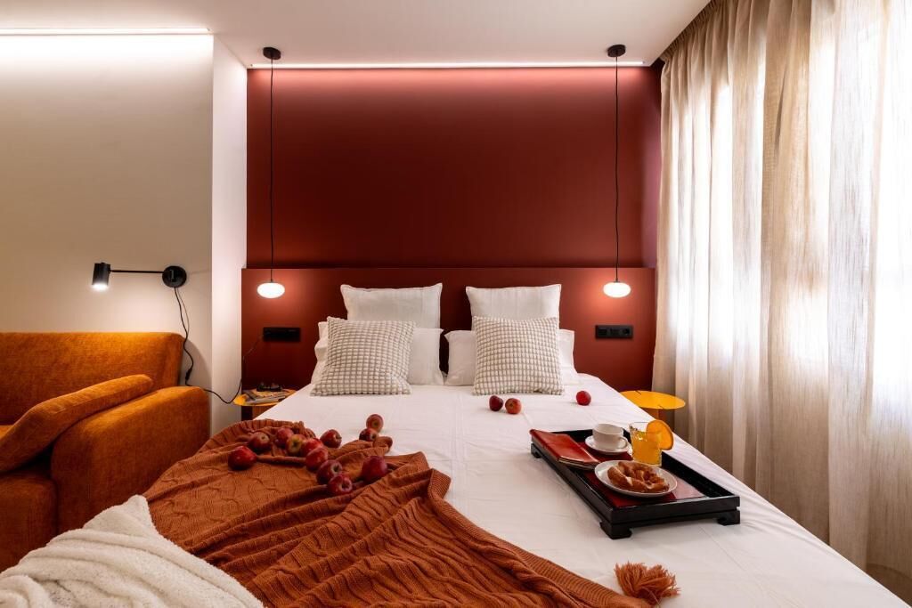 Habitación de hotel con una cama grande, un sofá, una bandeja con alimentos para el desayuno y una lámpara.