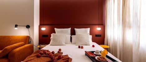 Habitación de hotel con una cama grande, un sofá, una bandeja con alimentos para el desayuno y una lámpara.