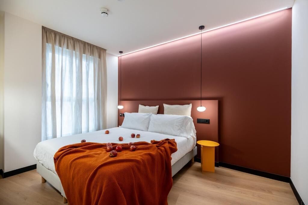 Un dormitorio moderno con cama, mesita de noche y ventana con cortinas.