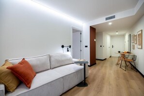 A modern living room with a sofa, a small table, and a chair. There is a door leading to another room and a hallway with a door at the end. - VORS&Co Jerez (Jerez de la Frontera)
