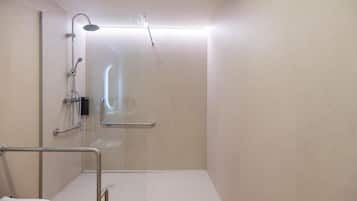A modern bathroom with a glass shower enclosure, a handrail, and a white sink.