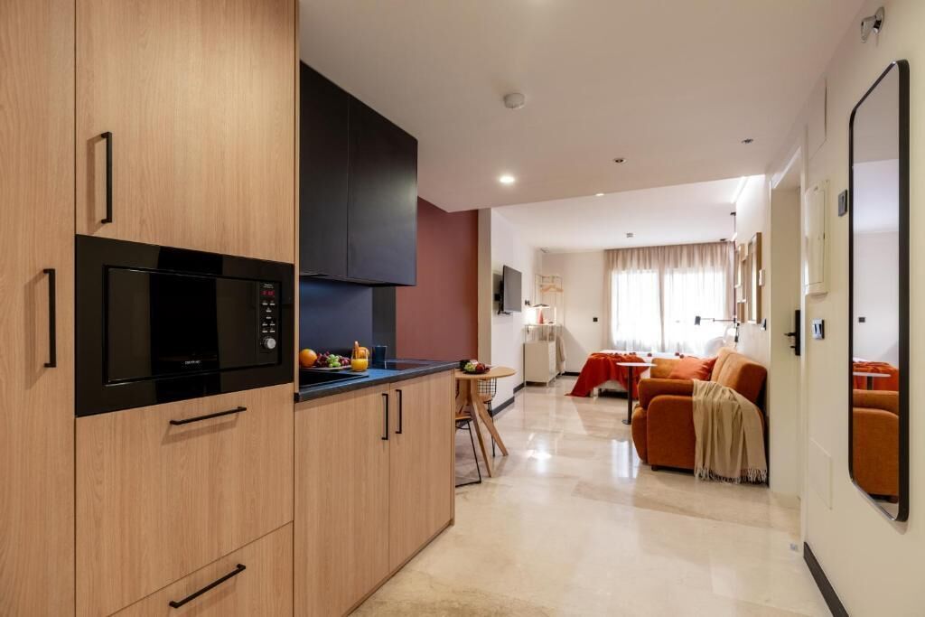 Une cuisine moderne équipée d’un four à micro-ondes, d’une cuisinière et de meubles de rangement en bois. On y trouve également un coin repas avec une table et des chaises, ainsi qu’un salon avec un canapé et un téléviseur.
