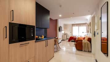 Une cuisine moderne équipée d’un four à micro-ondes, d’une cuisinière et de meubles de rangement en bois. On y trouve également un coin repas avec une table et des chaises, ainsi qu’un salon avec un canapé et un téléviseur.