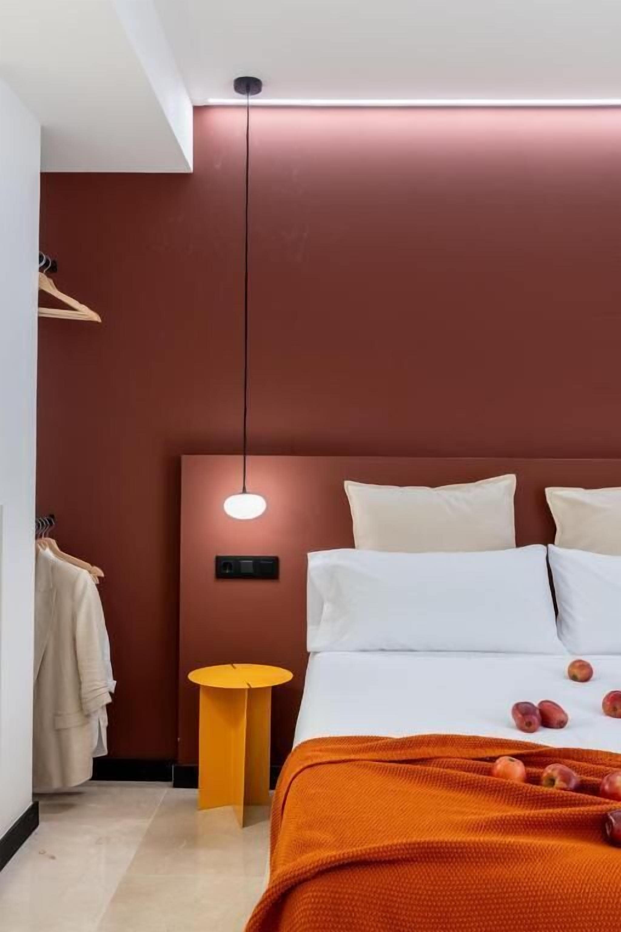 Una habitación de hotel con una cama, una mesita auxiliar redonda amarilla y un perchero.