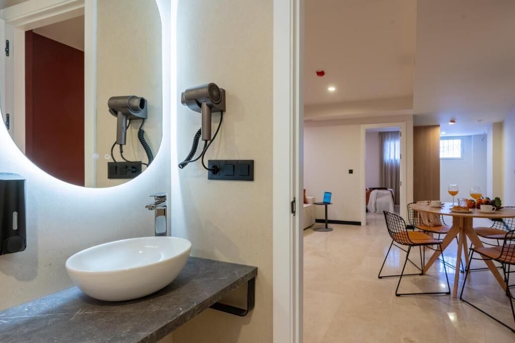 Un bany modern amb un mirall gran, un lavabo blanc i dos assecadors de cabell penjats a la paret.