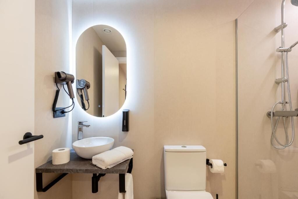 Et moderne badeværelse med et rundt spejl, en vask, et toilet og en bruser.