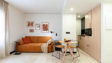 Een moderne woonkamer met een bank, een eettafel en een keuken met kasten en apparatuur.