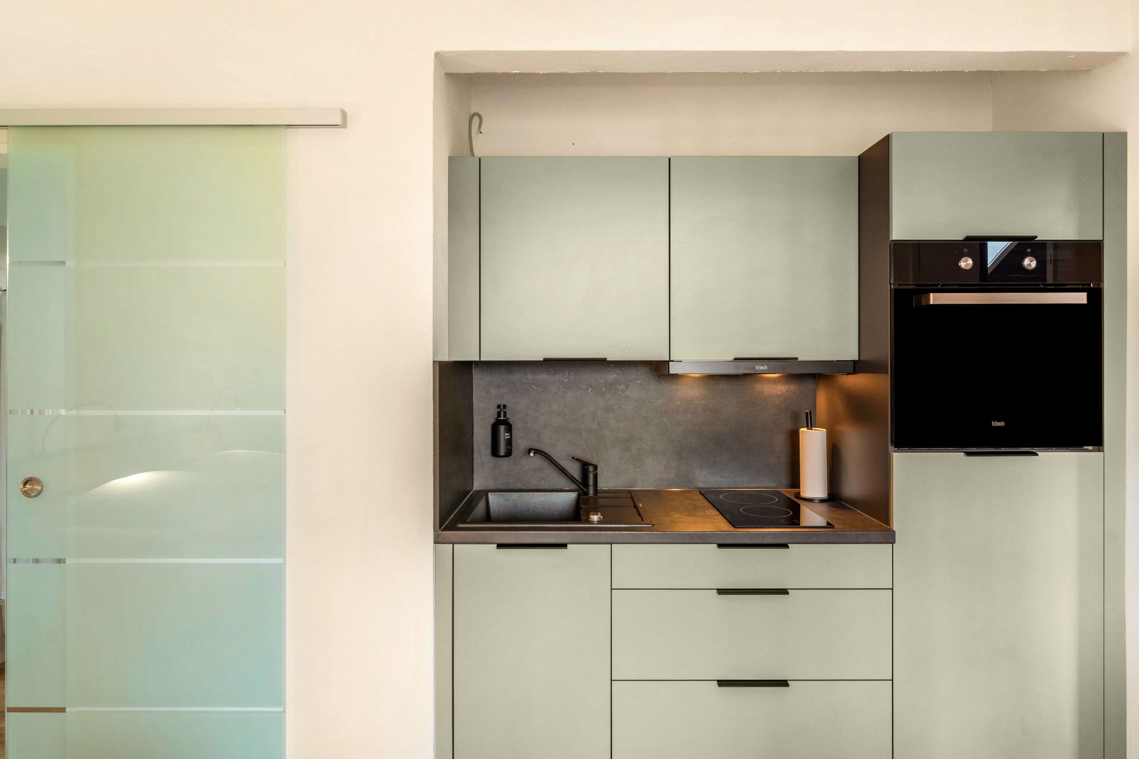 A compact kitchen with a built-in oven, a sink, and a coffee machine.