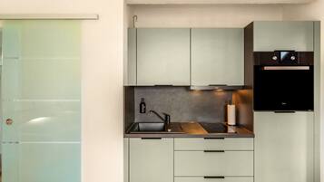 A compact kitchen with a built-in oven, a sink, and a coffee machine.