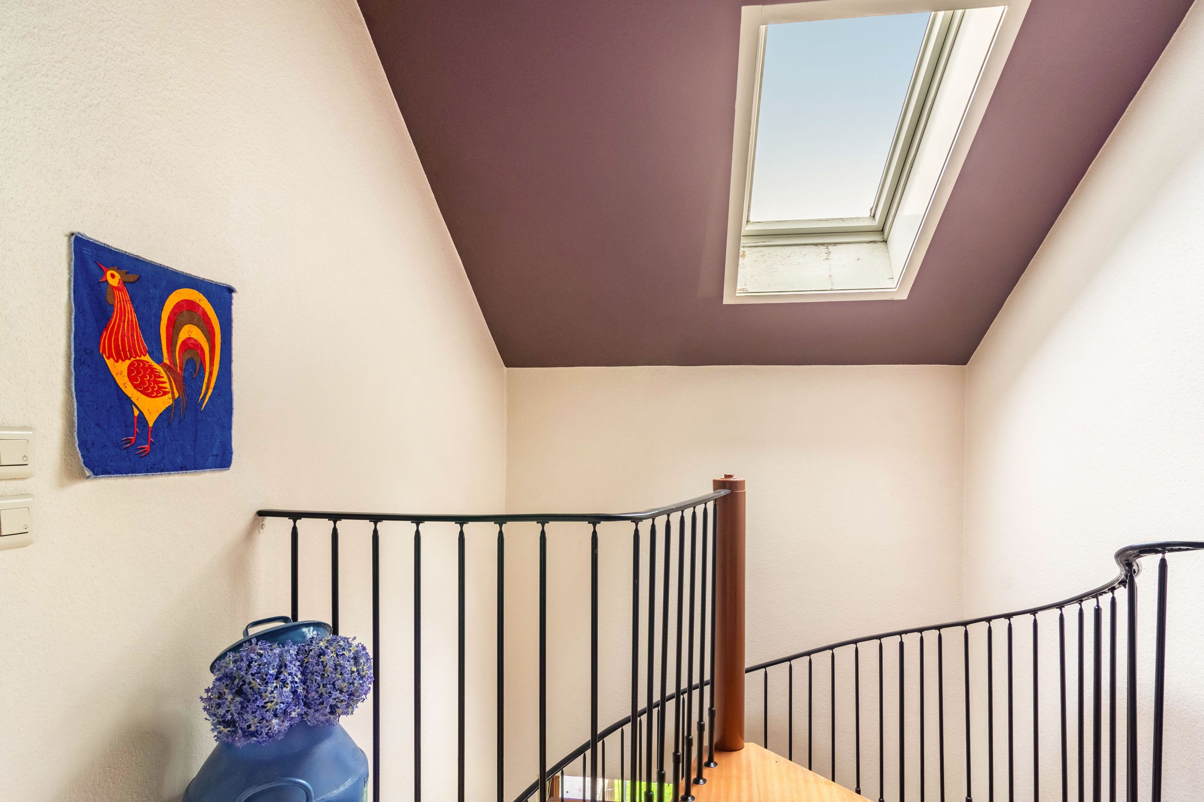 A staircase with a metal railing, a skylight, and a wall-mounted light switch.