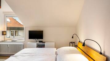 A bedroom with a bed, a TV, a bedside table, and a window with a view of a house.