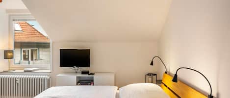 Une chambre à coucher avec un lit, une télévision, une table de chevet et une fenêtre donnant sur une maison.