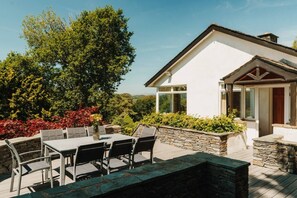 Ein modernes Haus mit einer Terrassenanlage, komplett mit Tisch und Stühlen, umgeben von Steinmauern und üppiger Vegetation.