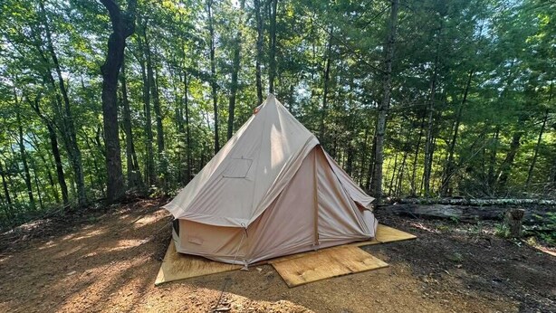A tent set up in a forested area with a dirt ground and wooden platform.