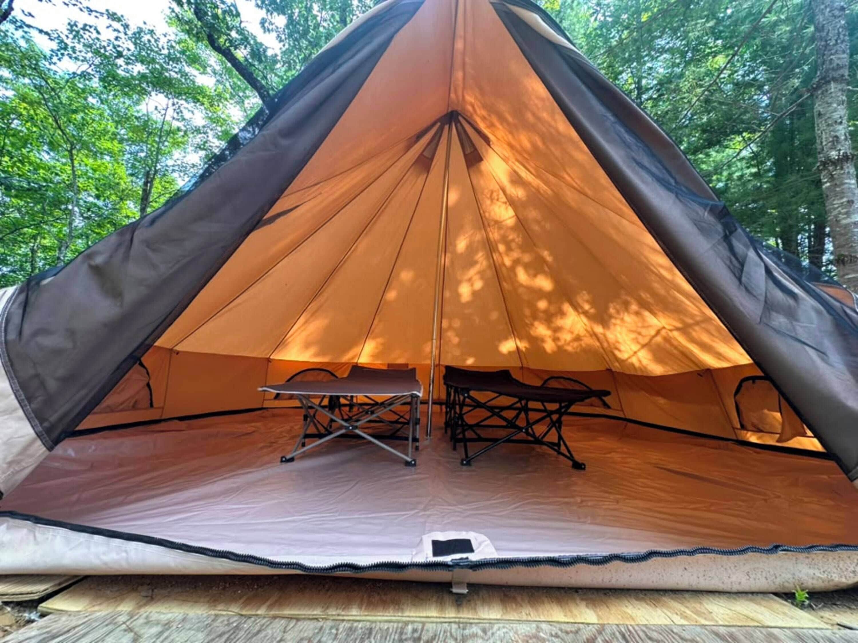 Een tent met een tafel en stoelen van binnen, omringd door bomen.