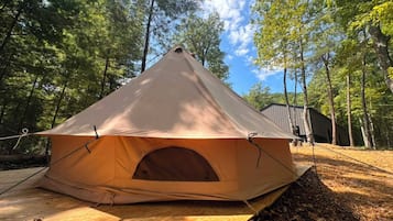 A dome-shaped tent with a central entrance, set up on a wooden platform in a forested area.