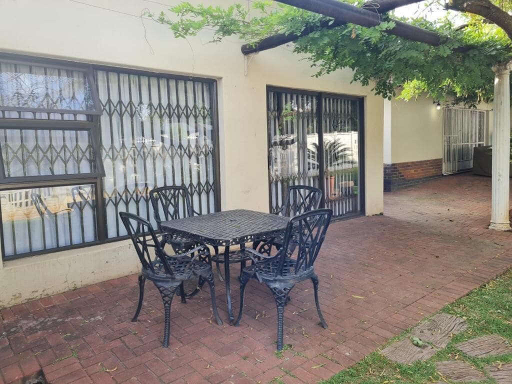 Un patio exterior con mesa y sillas, una zona cubierta con una pérgola y un acceso con portón.