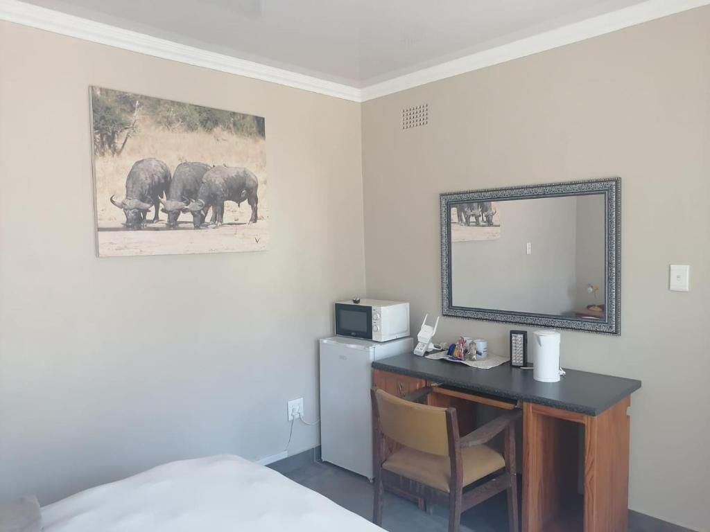 A hotel room with a bed, a desk with a chair, a microwave, a refrigerator, a large mirror, and a painting of elephants.