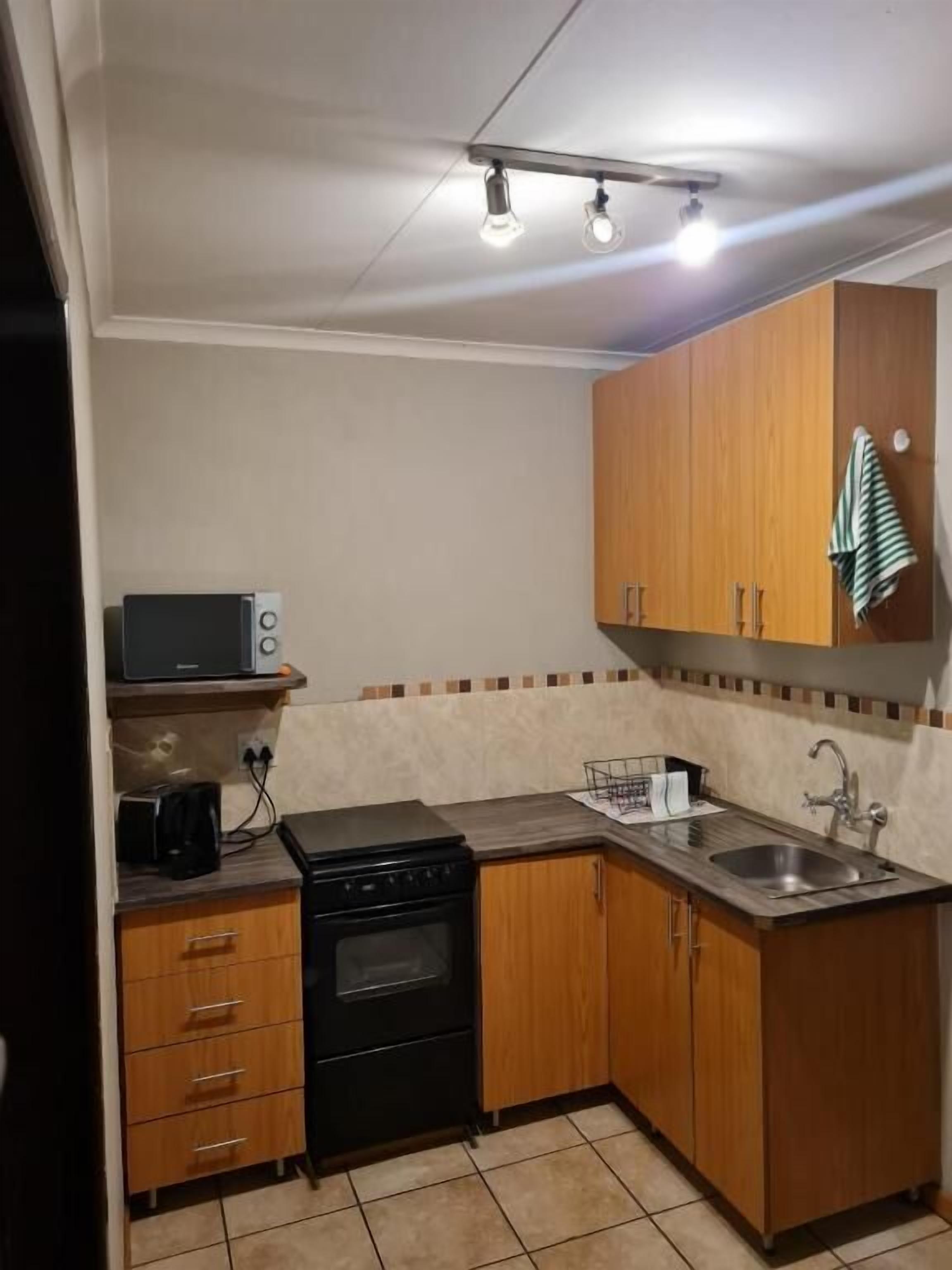 Una cocina compacta con armarios de madera, una estufa negra, un fregadero y un microondas.