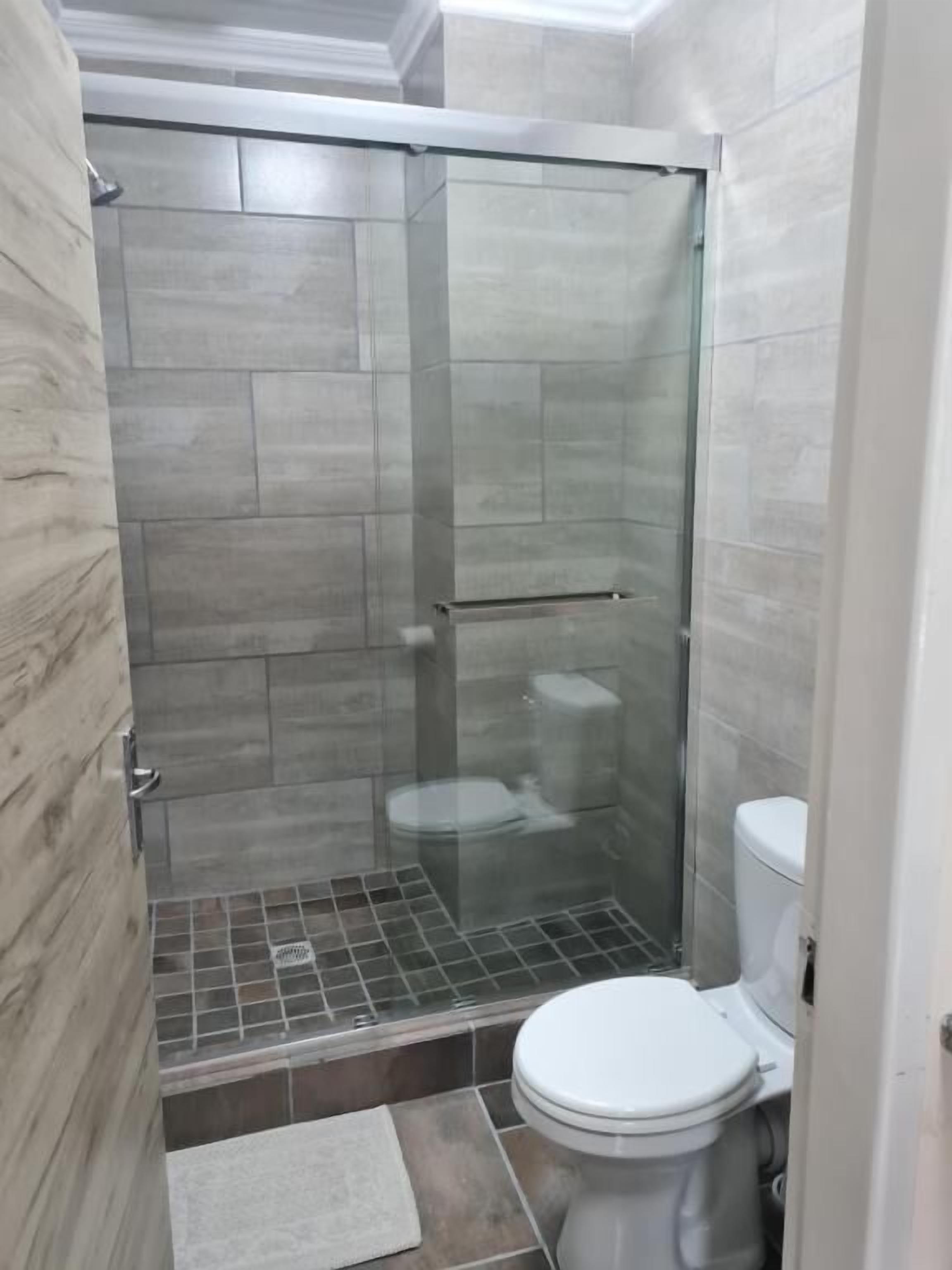 Un baño con ducha de vidrio, inodoro y piso de baldosas.