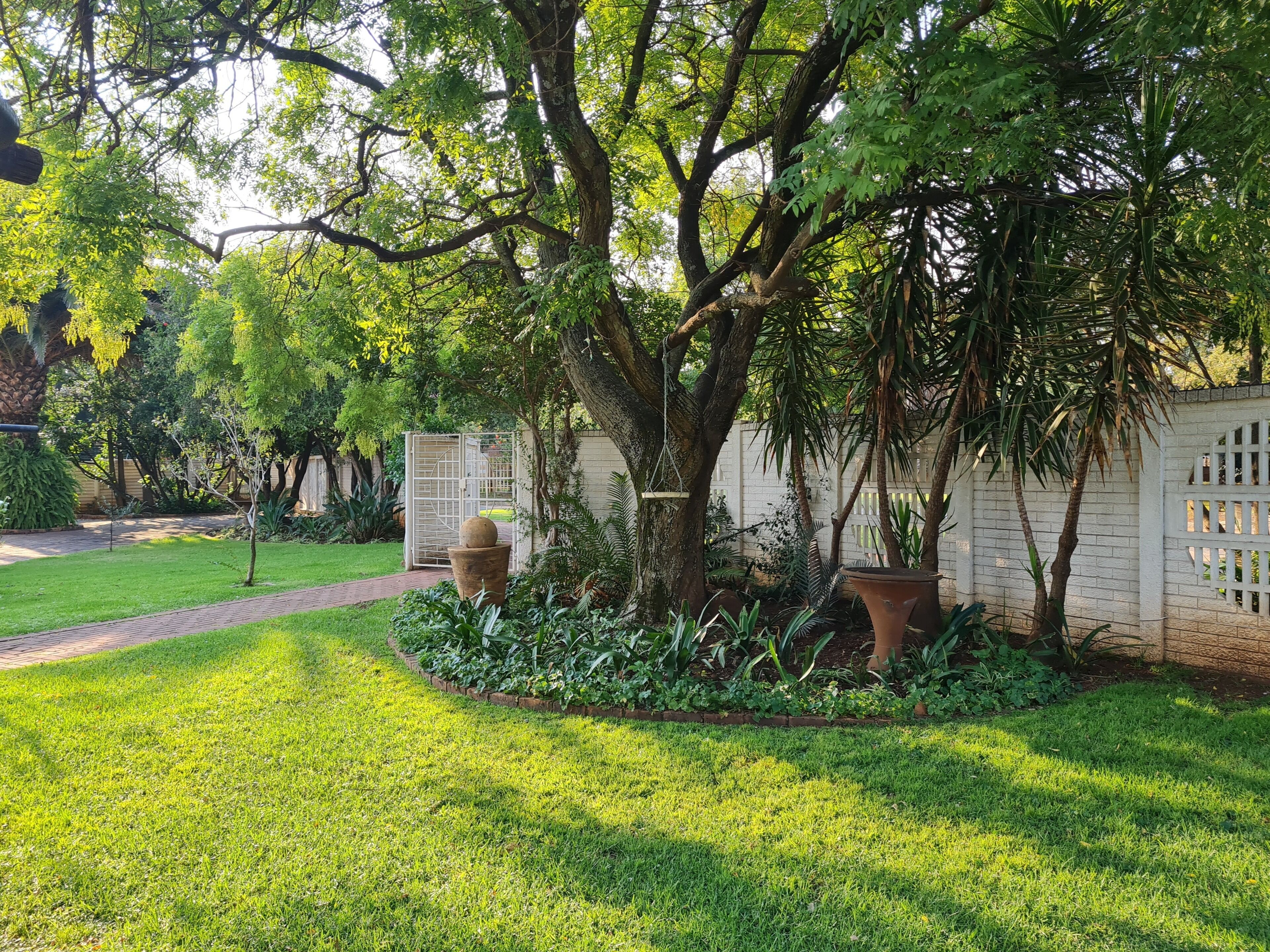 Un jardín cuidado con varios árboles, un sendero de ladrillo y una cerca blanca.