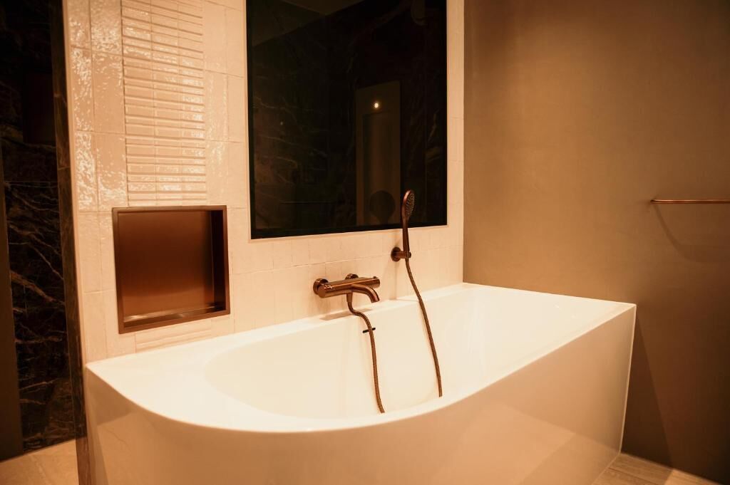 A modern bathroom with a freestanding bathtub, a window, and a marble wall.
