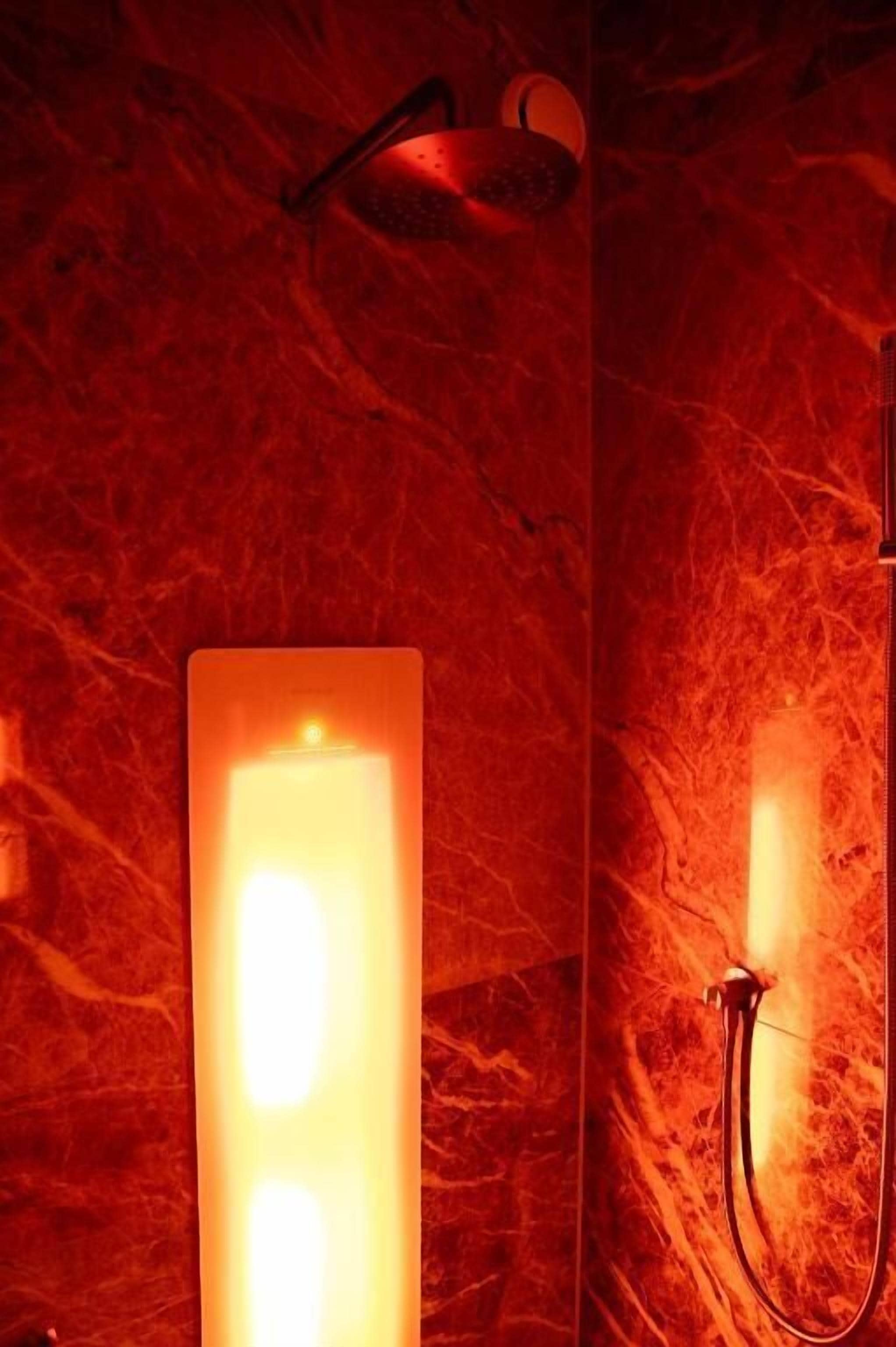 A bathroom with a red marble wall, a vertical light fixture, and a shower head.