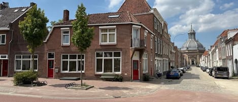 Une vue de rue avec des bâtiments traditionnels en briques, un ciel dégagé et des voitures garées.