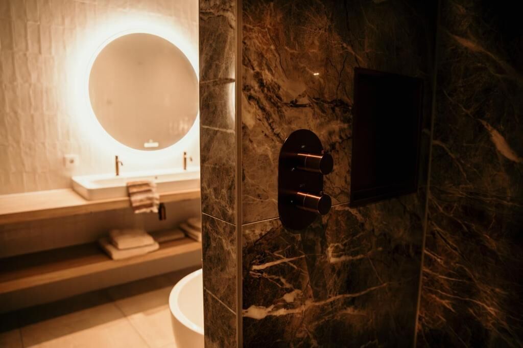 Een badkamer met een marmeren wand, een ronde spiegel, een wastafel en een toilet.