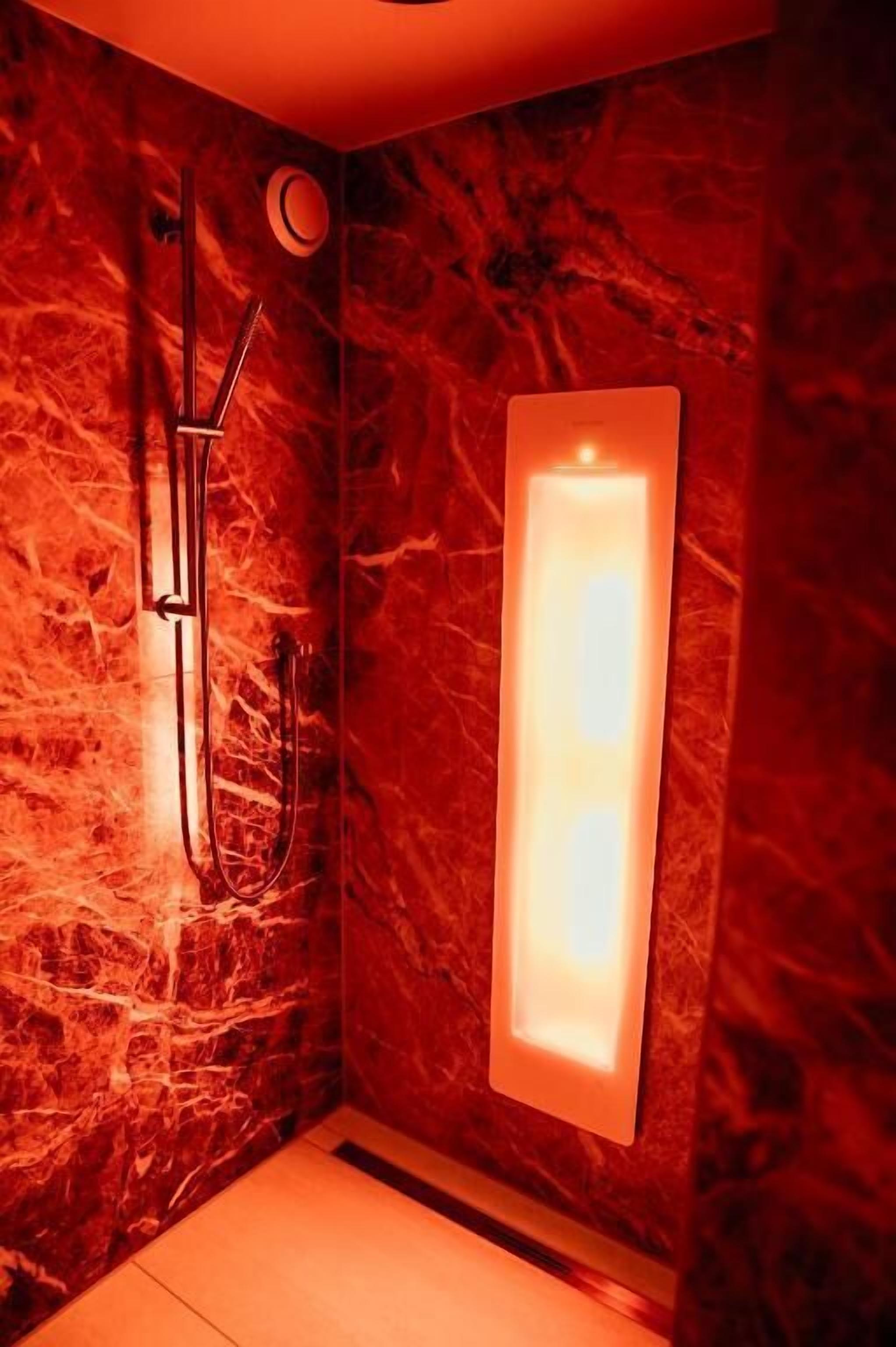 A bathroom with a marble wall, a shower, and a lit wall-mounted light fixture.