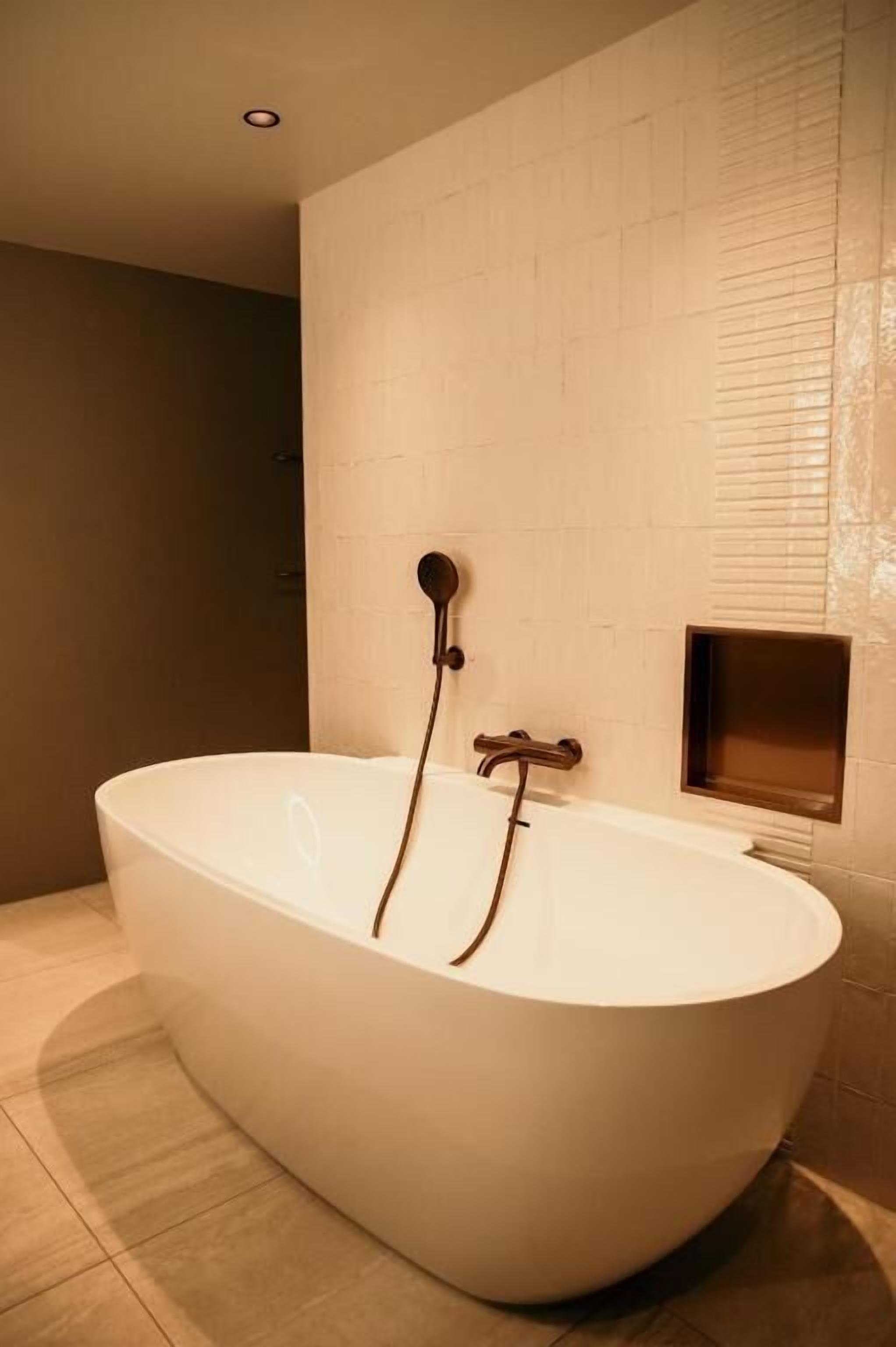 Un baño moderno con una bañera independiente, un cabezal de ducha empotrado y un espejo rectangular pequeño.