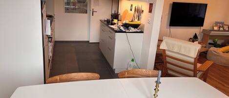 Una cocina moderna con armarios blancos, una mesa de comedor con una vela y un televisor montado en la pared.