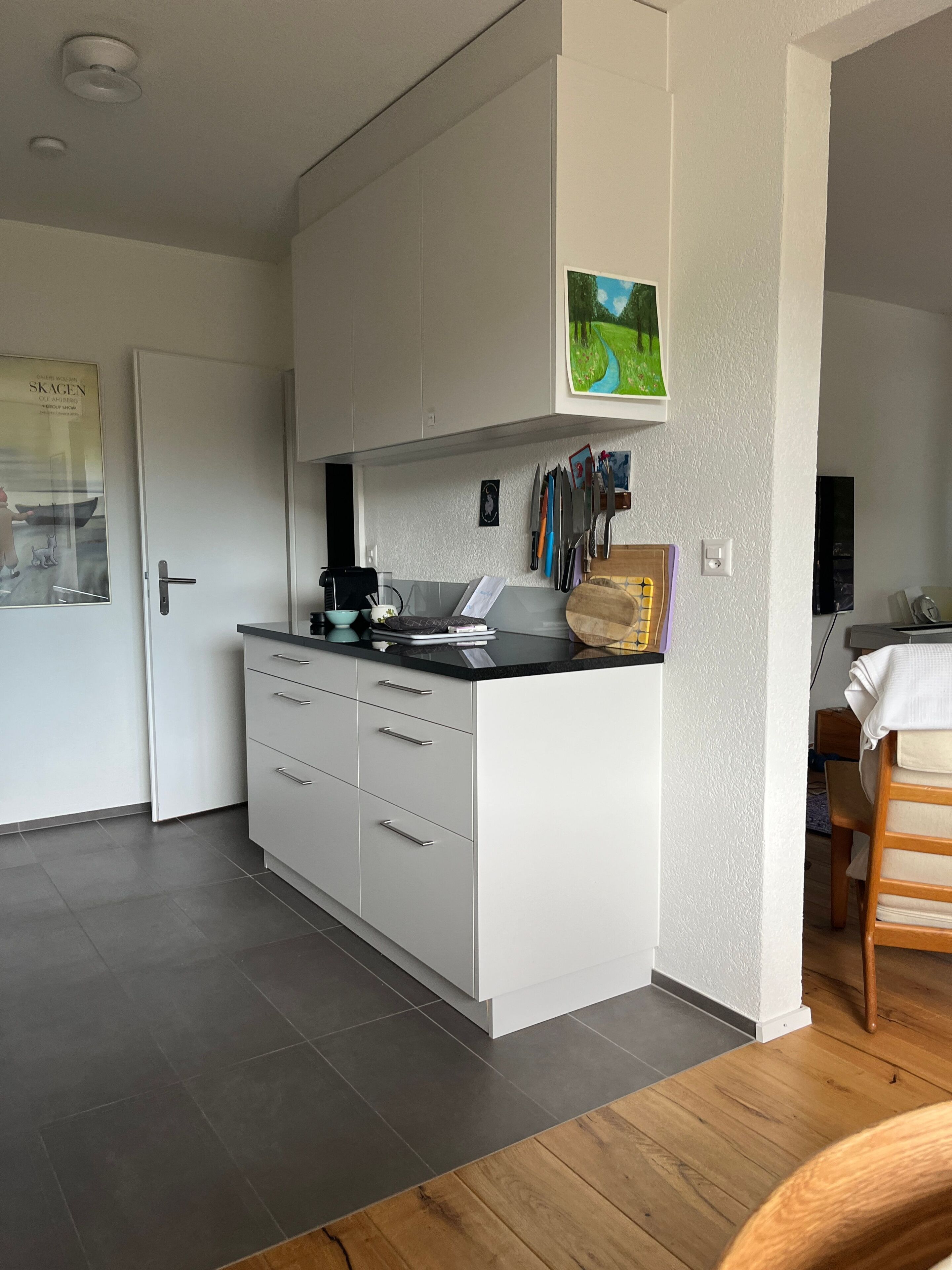 A modern kitchen with white cabinetry, a black countertop, and a wooden chair.