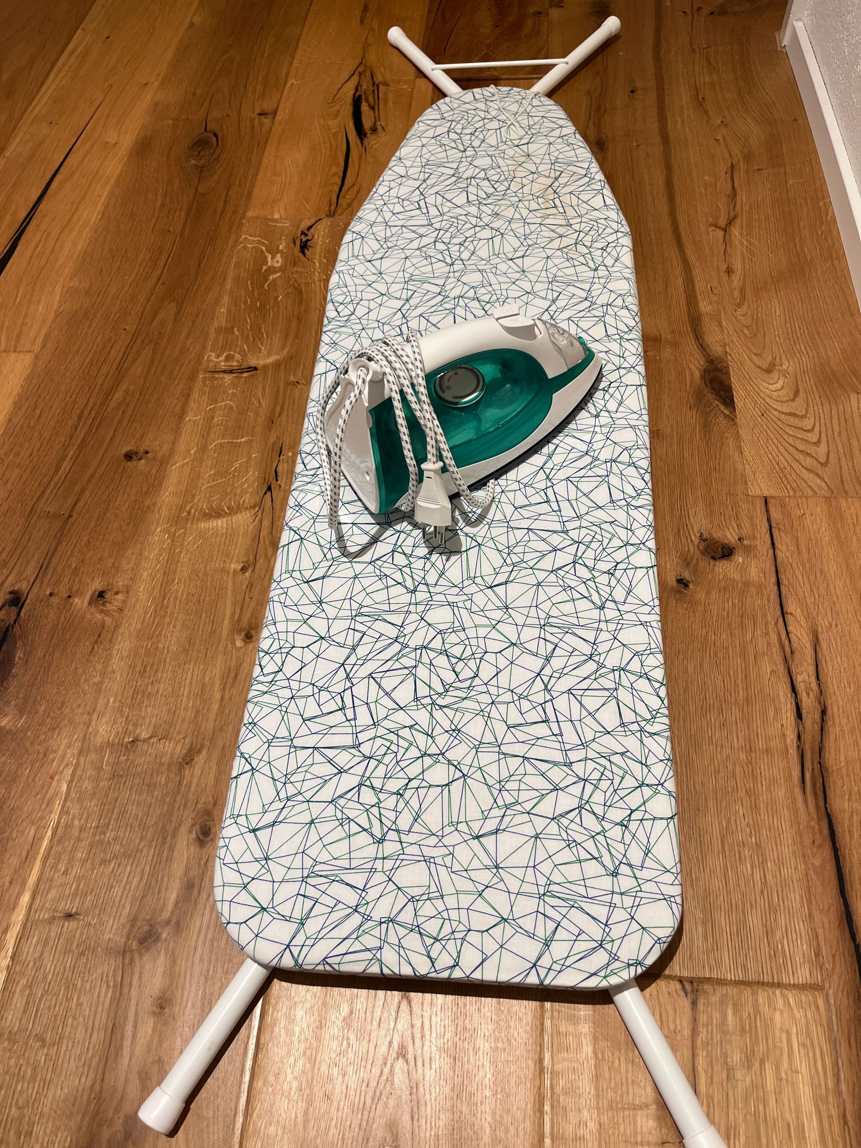 An ironing board with an iron and a cord on a wooden floor.