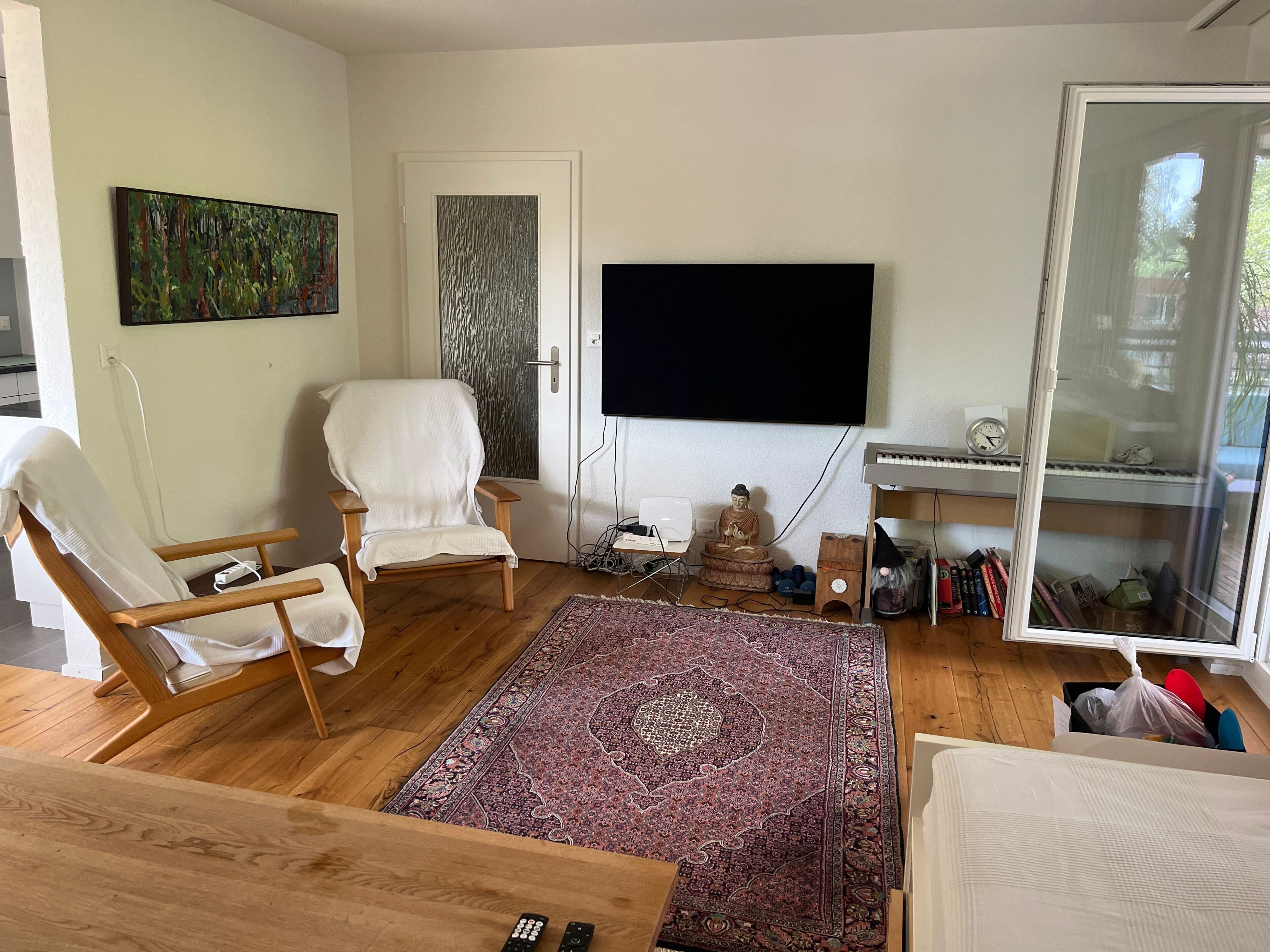 A living room with a large flat-screen TV, a white armchair, a wooden coffee table, and a patterned rug.