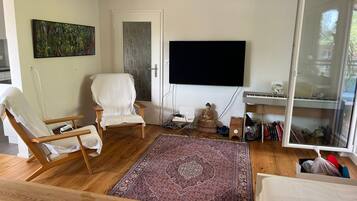 A living room with a large flat-screen TV, a white armchair, a wooden coffee table, and a patterned rug.