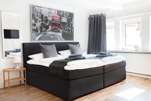 A modern bedroom with a black sofa bed, a flat-screen TV mounted on the wall, a framed cityscape photo, and a window with curtains. - Townhouse Duderstadt: Studio 2 (Duderstadt)