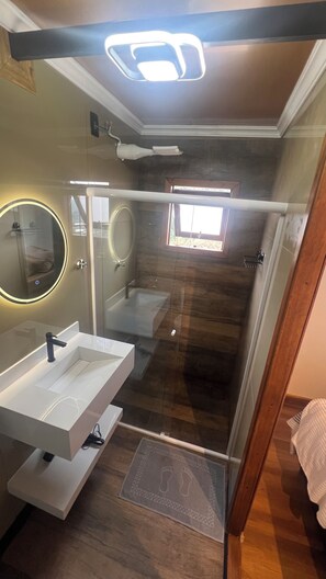 A modern bathroom with a glass shower enclosure, a vanity with a mirror, and a ceiling light fixture.