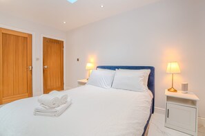 Een hotelkamer met een net opgemaakt bed, een houten deur, twee nachtkastjes met lampen, en een klein kastje.