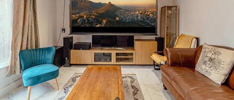 A living room with a large flat-screen TV, a blue armchair, a brown sofa, and a wooden coffee table.