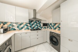 Een moderne keuken met witte kastjes, een decoratieve achterwand, een ingebouwde kookplaat, een wasmachine en een magnetron.