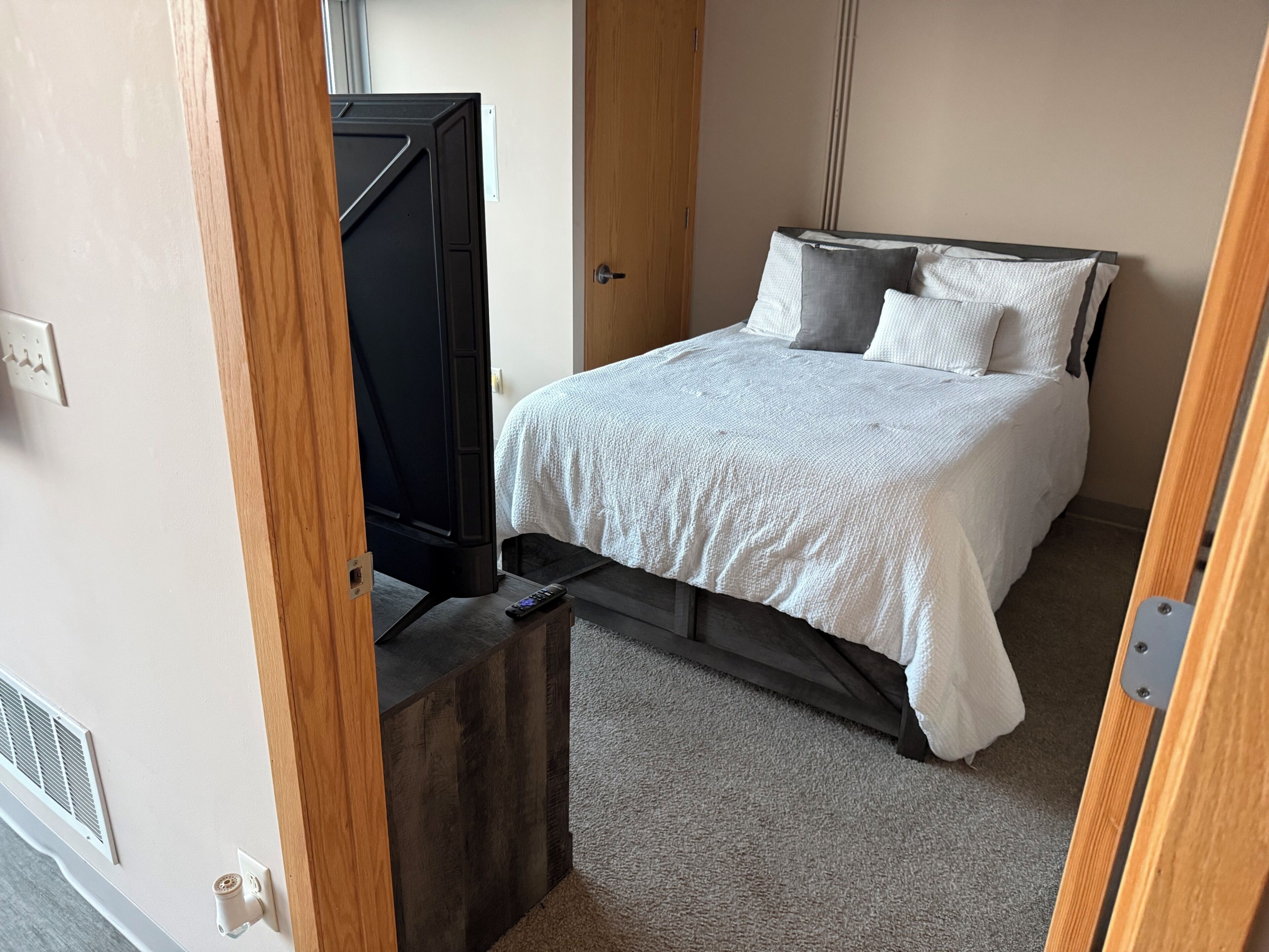 A bedroom with a bed, a television, and a wooden door.