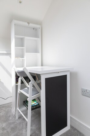 Un bureau blanc avec un panneau noir, une étagère blanche et un sol recouvert d’un tapis gris.