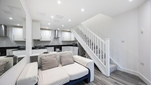 A modern kitchen with white cabinets, a central island, and a staircase leading to an upper level.