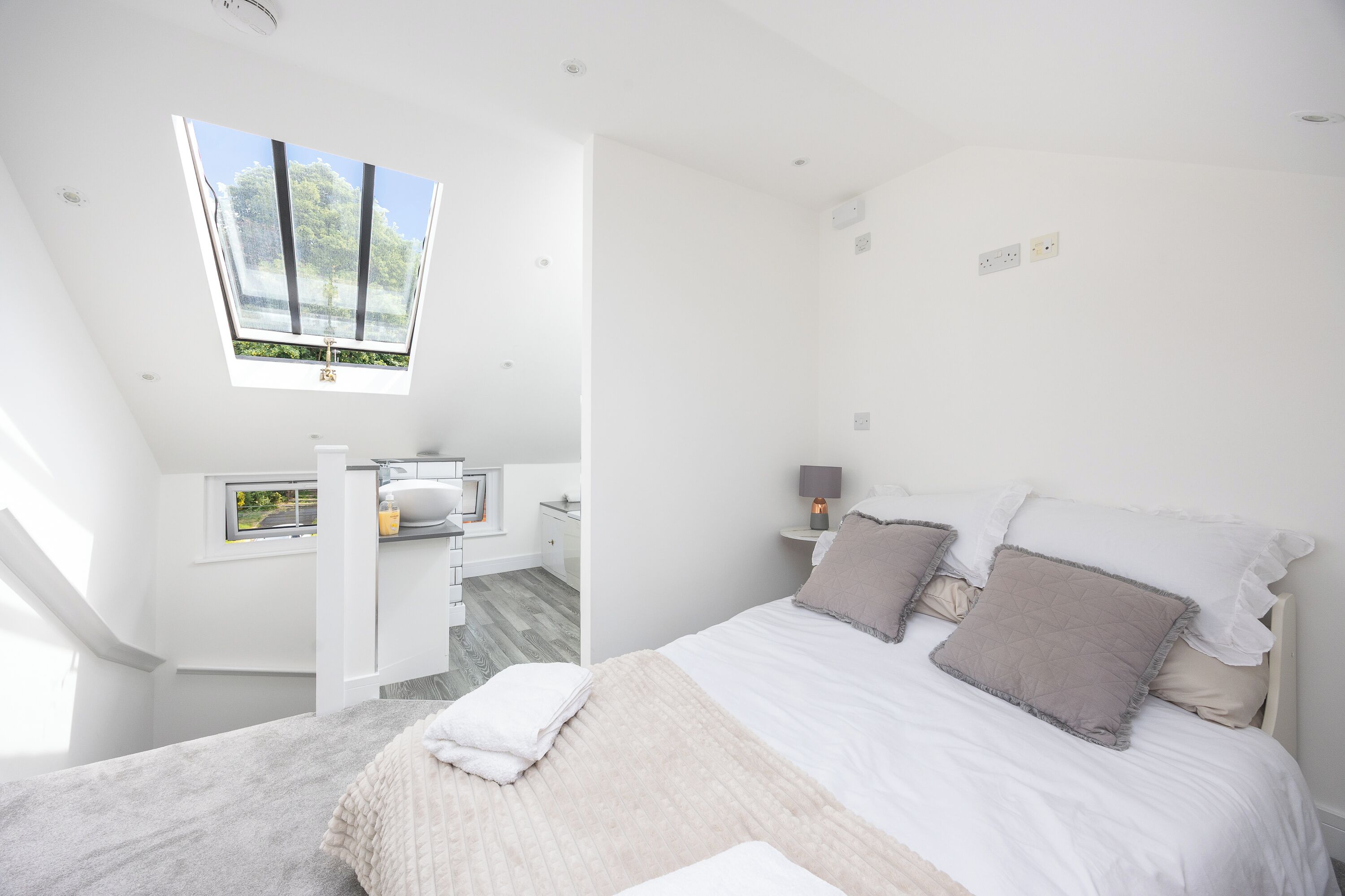 A bedroom with a bed, a window, a small bathroom, and a view of greenery outside.