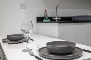 Une cuisine au style minimaliste, avec un plan de travail blanc, un verre à vin et de la vaisselle grise.