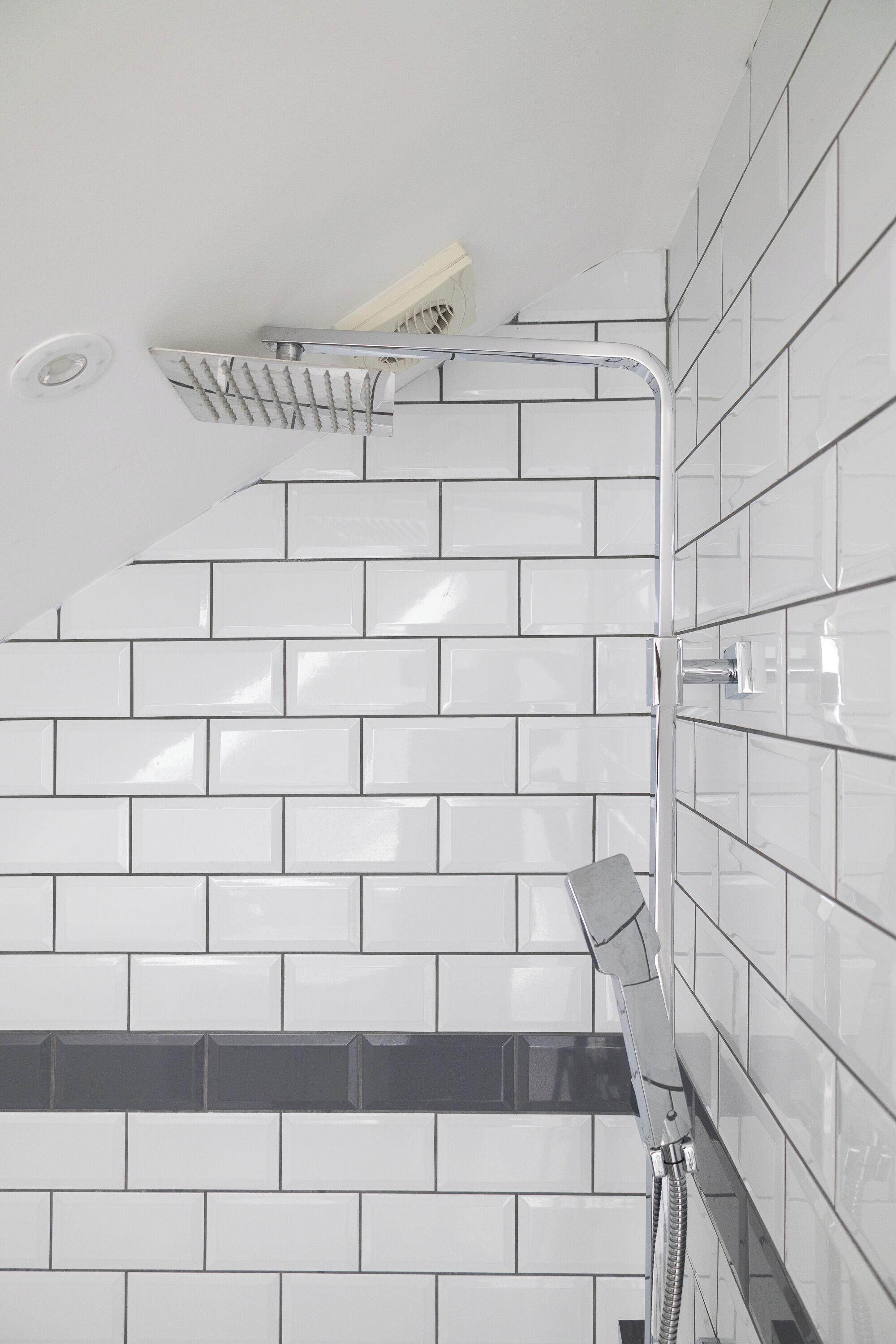 A bathroom with white tiled walls, a shower with a chrome faucet, and a visible drain.