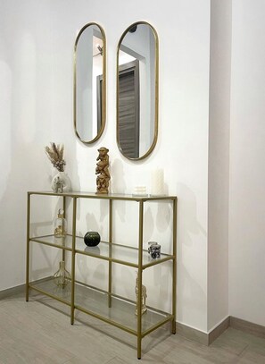 A room with a gold-framed console table against a white wall, featuring a vase, a decorative sculpture, and a mirror.