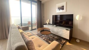 Ein modernes Wohnzimmer mit großem Flachbildfernseher, einer Couch, einem Couchtisch und Meerblick durch große Fenster.